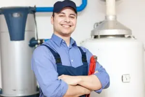 Plumber standing confidently with a wrench, showcasing tank and tankless water heaters in a service environment.