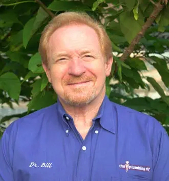 Dr. Bill, owner of The Plumbing Dr, smiling in a blue work shirt, surrounded by greenery, representing the Falls Church plumbing team.