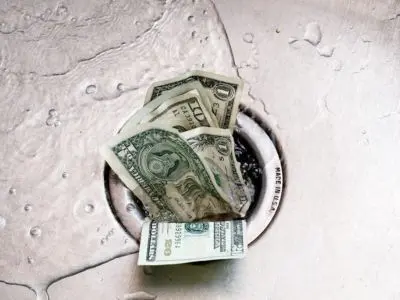 Dollar bills partially submerged in water near a drain, symbolizing wasted money due to water leaks and high water bills.