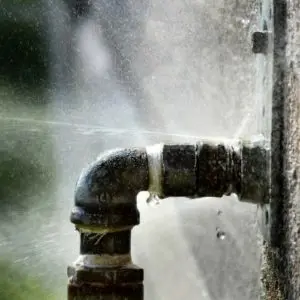 Burst water pipe spraying water, illustrating plumbing emergency in residential settings.