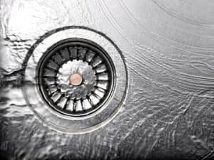 Garbage disposal drain with water flowing, highlighting potential leakage issues in kitchen plumbing.