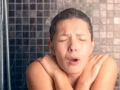 Woman in shower with a shocked expression, experiencing cold water, highlighting inadequate hot water supply issues related to water heaters.