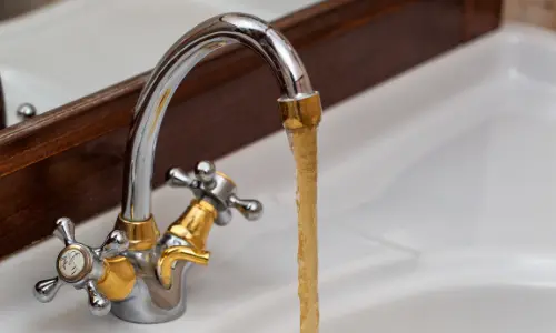 Rust-colored water flowing from a faucet, indicating potential water heater issues and rust formation.