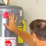 Person inspecting a water heater, touching the performance indicator, emphasizing maintenance and replacement for optimal efficiency in plumbing services.