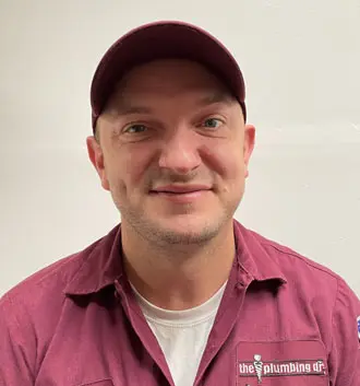 Dr. Brandon, plumbing technician at The Plumbing Dr., smiling in uniform with company logo, showcasing expertise and commitment to plumbing services.