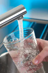 Water pouring from a faucet into a clear glass, emphasizing the importance of clean drinking water and the benefits of a whole-house water filtration system.