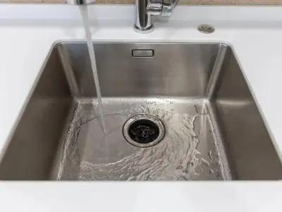 Water running through a stainless steel sink, illustrating proper maintenance for garbage disposal systems.