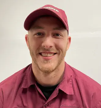 Smiling plumber assistant wearing a maroon uniform and cap, representing The Plumbing Dr, showcasing a friendly demeanor and professionalism.
