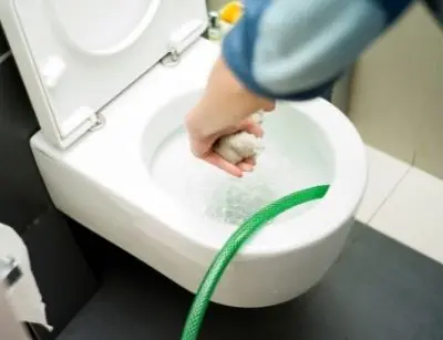 Person using a plunger on an overflowing toilet, illustrating a common plumbing emergency related to clogs and the need for professional plumbing services.