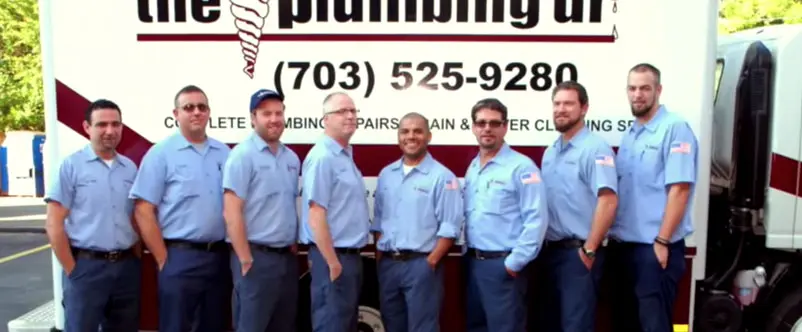 Team of plumbers from The Plumbing Dr, wearing blue uniforms, standing in front of service vehicle, showcasing expertise in plumbing services.