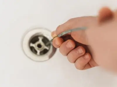 Hand using a drain snake to clear a clog from a sink drain, illustrating professional plumbing techniques for effective drain cleaning.