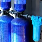 Whole-house water filtration system with blue tanks and a filter, highlighting water safety and quality improvements for homes.