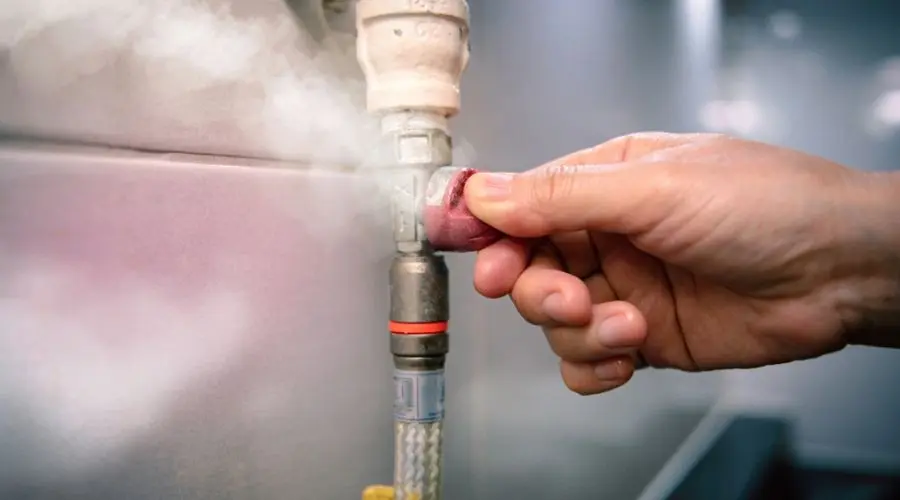 Hand adjusting a valve on a plumbing pipe with steam escaping, illustrating plumbing maintenance and potential water leak issues.