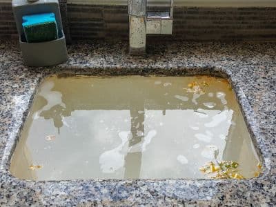 Clogged kitchen sink with standing dirty water and debris, indicating the need for professional drain cleaning services.