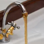 Rust-colored water flowing from a faucet, indicating potential water heater distress, relevant to plumbing issues discussed by The Plumbing Dr in Falls Church, VA.
