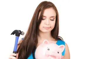 Woman holding a hammer and a piggy bank, illustrating the potential costs of DIY plumbing repairs versus hiring a professional plumber.