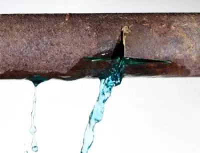 Rusty pipe with a visible burst, leaking water, illustrating plumbing emergencies and the dangers of burst pipes.