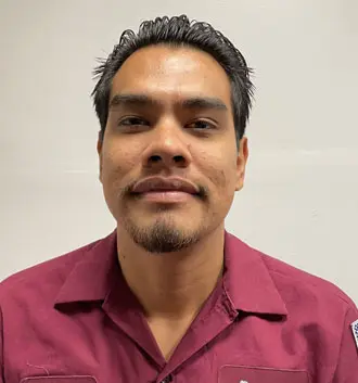 Plumber assistant Dr. Marcelo in a maroon work shirt, smiling against a plain background, representing The Plumbing Dr team and their commitment to customer service.