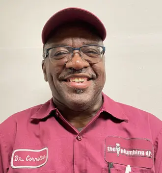 Dr. Cornelius, plumber assistant at The Plumbing Dr, smiling in a maroon uniform with logo, showcasing friendly personality and expertise in plumbing service and repair.