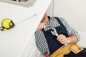 Commercial plumber working under a sink with adjustable wrench, showcasing plumbing services for businesses.
