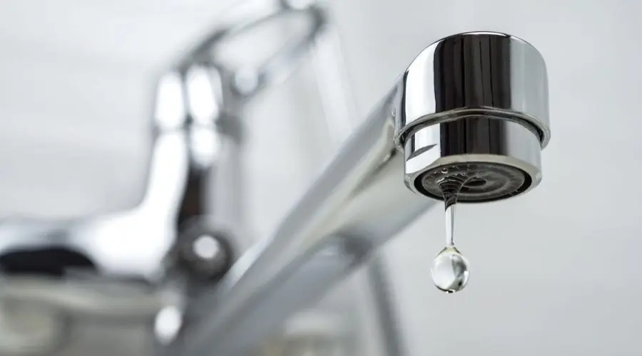 Close-up of a chrome faucet with a single water droplet forming at the tip, illustrating plumbing issues related to leaks and water hammer.