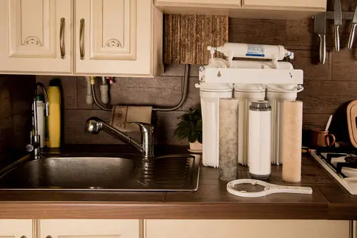 Water filtration system installed under kitchen sink, featuring multiple filter cartridges and a faucet, highlighting the importance of clean drinking water for health and well-being.