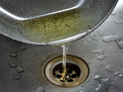 Cooking grease pouring from a pan into a sink drain, illustrating common causes of sewer line clogs and the importance of proper disposal to prevent plumbing issues.