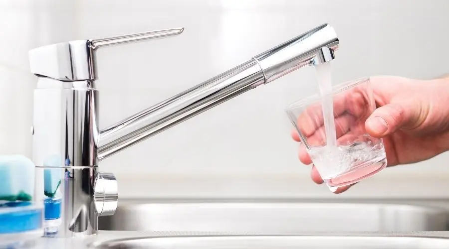 Modern kitchen faucet dispensing water into a glass, highlighting the importance of water quality and filtration for homeowners.