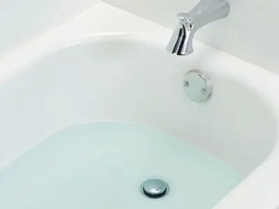 Bathtub with standing water indicating slow drainage, suggesting potential sewer line clog issues related to plumbing problems.