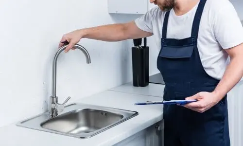 Plumber inspecting kitchen faucet and sink during plumbing inspection service.