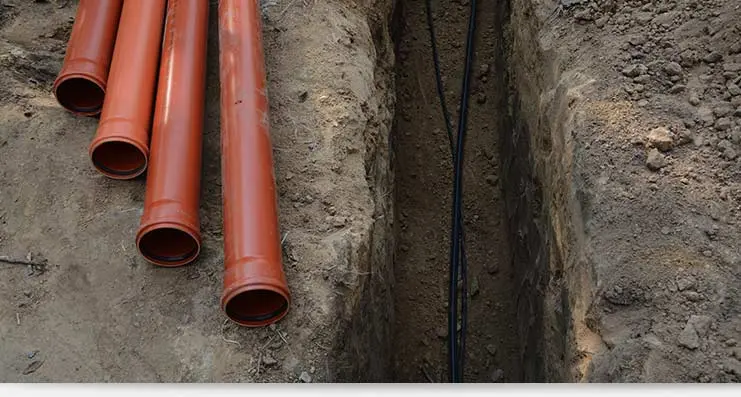 Excavation site showing orange pipes and a trench for plumbing installation, illustrating Lodder Brothers Limited's excavation services for residential and commercial needs.