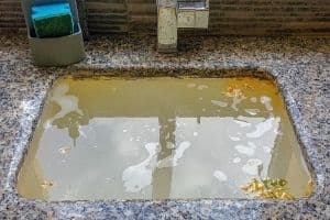 Overflowing sink with murky water and debris, illustrating plumbing emergency and potential clog issues.