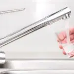 Modern kitchen faucet pouring water into a glass, showcasing whole-home water filtration by Charles Krull & Son, Inc.