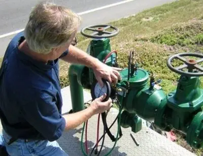 Professional performing backflow testing on green plumbing equipment, ensuring safe water supply and compliance with certification standards.
