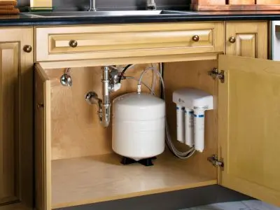 Under-sink water filtration system with a white tank and multiple filters, showcasing plumbing setup for clean drinking water in a kitchen environment.