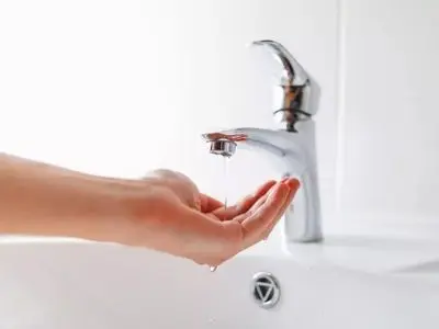 Hand catching a trickle of water from a bathroom faucet, illustrating low water pressure issues related to plumbing leaks.
