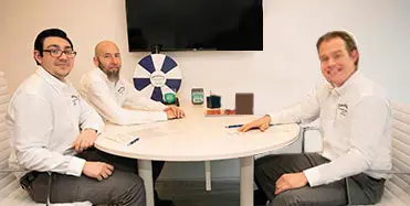 Three professionals at a round table discussing plumbing and heating solutions with a white spinning wheel in Malverne, NY.