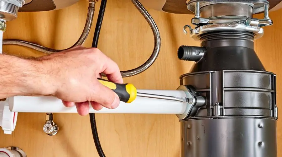 Hand using a screwdriver to repair a garbage disposal under a kitchen sink, highlighting plumbing maintenance and repair tasks.