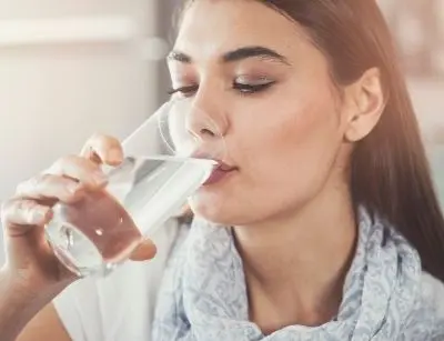 Woman drinking clear water from a glass, emphasizing improved taste and quality from a whole-home water filtration system.