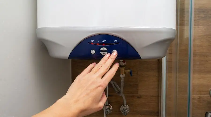 Water heater unit with digital display and temperature dial being adjusted by hand for home maintenance.