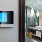 Smart thermostat in a clean bathroom with a sink and mirror, showcasing modern HVAC design by Charles Krull & Son, Inc.