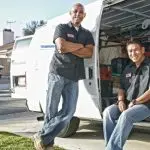 Two plumbers in uniforms beside a service van showcasing essential plumbing tools and equipment.