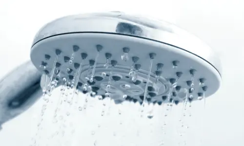 Showerhead with water droplets illustrating fluctuating water temperature issues in plumbing systems.
