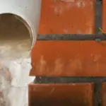 Drainage pipe pouring water onto rough brick flooring, highlighting plumbing maintenance for preventing frozen pipes.