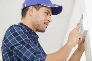 Technician adjusting a thermostat, emphasizing HVAC maintenance and troubleshooting solutions for home comfort.
