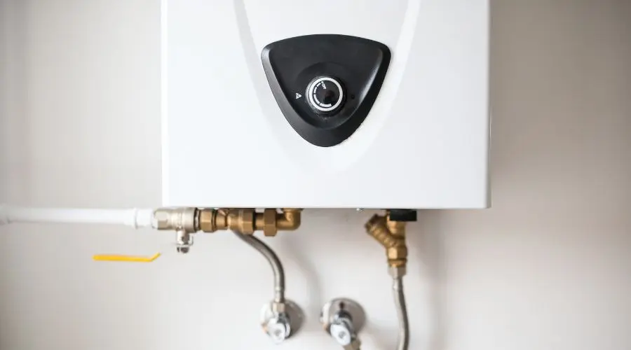 Wall-mounted water heater with black control knob, metal pipes, and valves from Charles Krull & Son, Inc. Plumbing & Heating.