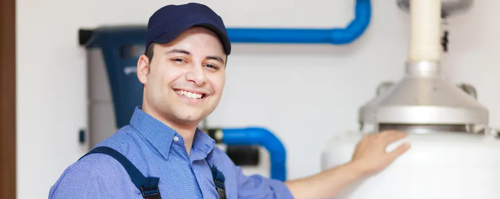 Smiling male technician in blue cap servicing a water heater for plumbing by Charles Krull & Son, Inc.