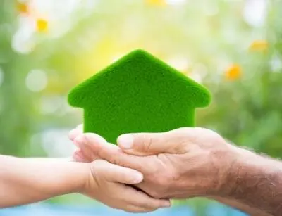 Hands holding a green, eco-friendly house symbol, representing sustainable home heating and boiler efficiency in a residential context.