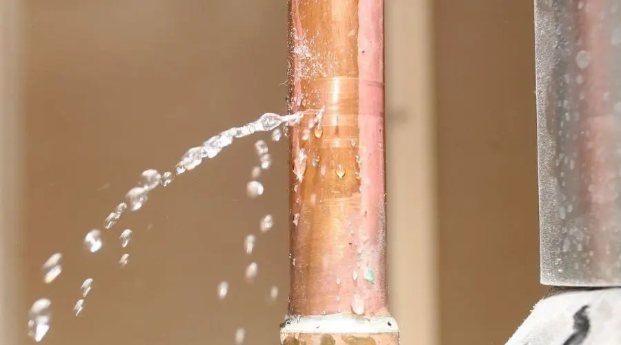 Water spraying from a copper pipe in a plumbing maintenance area, showcasing urgent plumbing issues.
