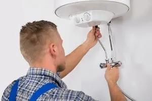 Plumber performing maintenance on a water heater, adjusting pipes and connections, emphasizing routine plumbing services for water heater issues.